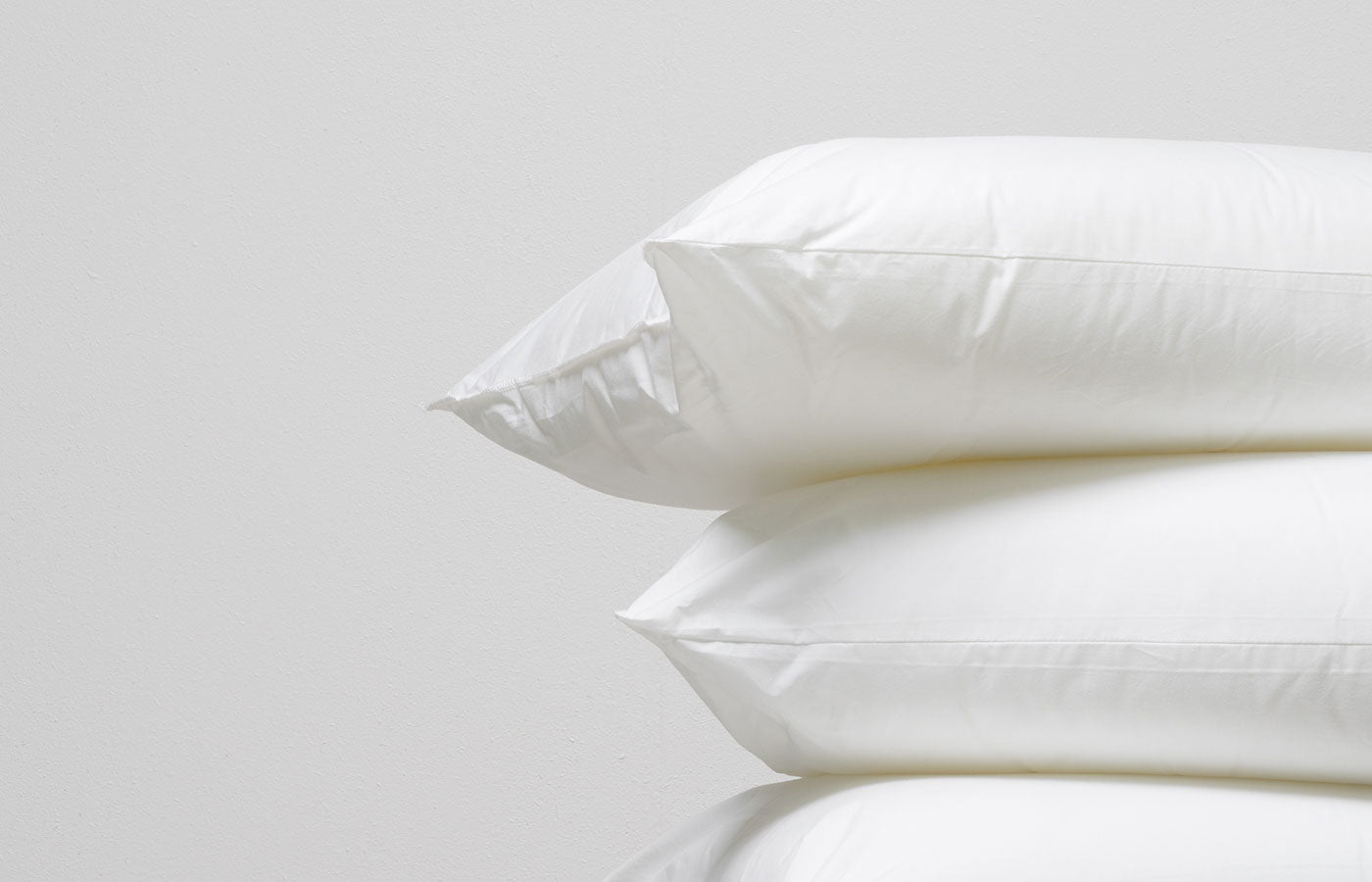 Stacked white Australian-made pillows against a neutral grey background.