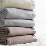 A stack of folded Australian washable wool blankets in ivory, platinum grey, and angora brown, with satin borders.
