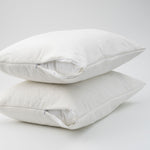 Two white waterproof bamboo pillow protectors fitted over pillows with partially opened zip closures, stacked on a white background.