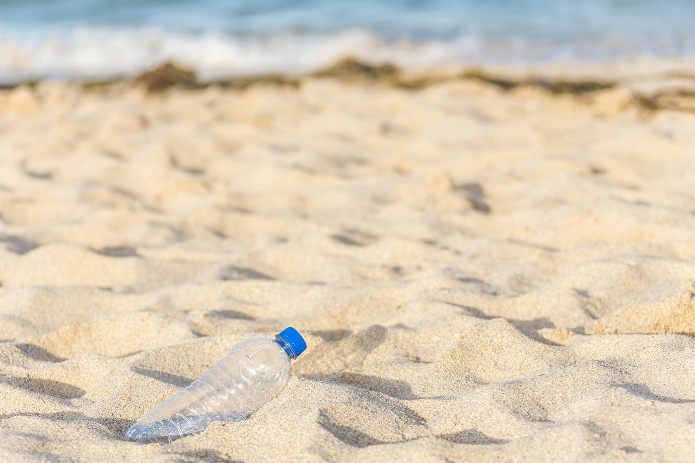 Plastic bottle on a sandy beach with ocean waves in the background