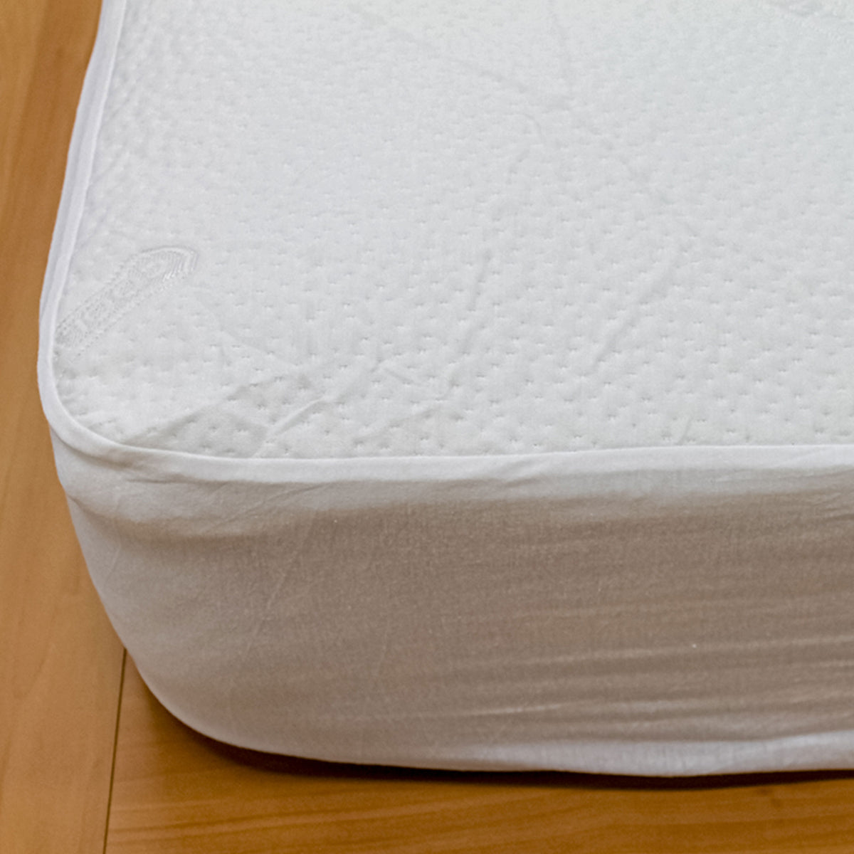 Close-up of a white CoolMax mattress protector with a jacquard-knit cover and fitted skirt over a mattress corner.