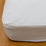 Close-up of a white CoolMax mattress protector with a jacquard-knit cover and fitted skirt over a mattress corner.