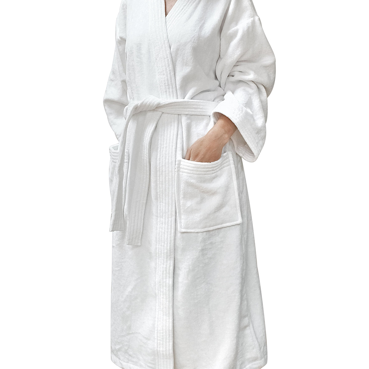 White cotton velour kimono-style bathrobe with a belt tie and patch pockets, modelled with one hand in a pocket against a white background.