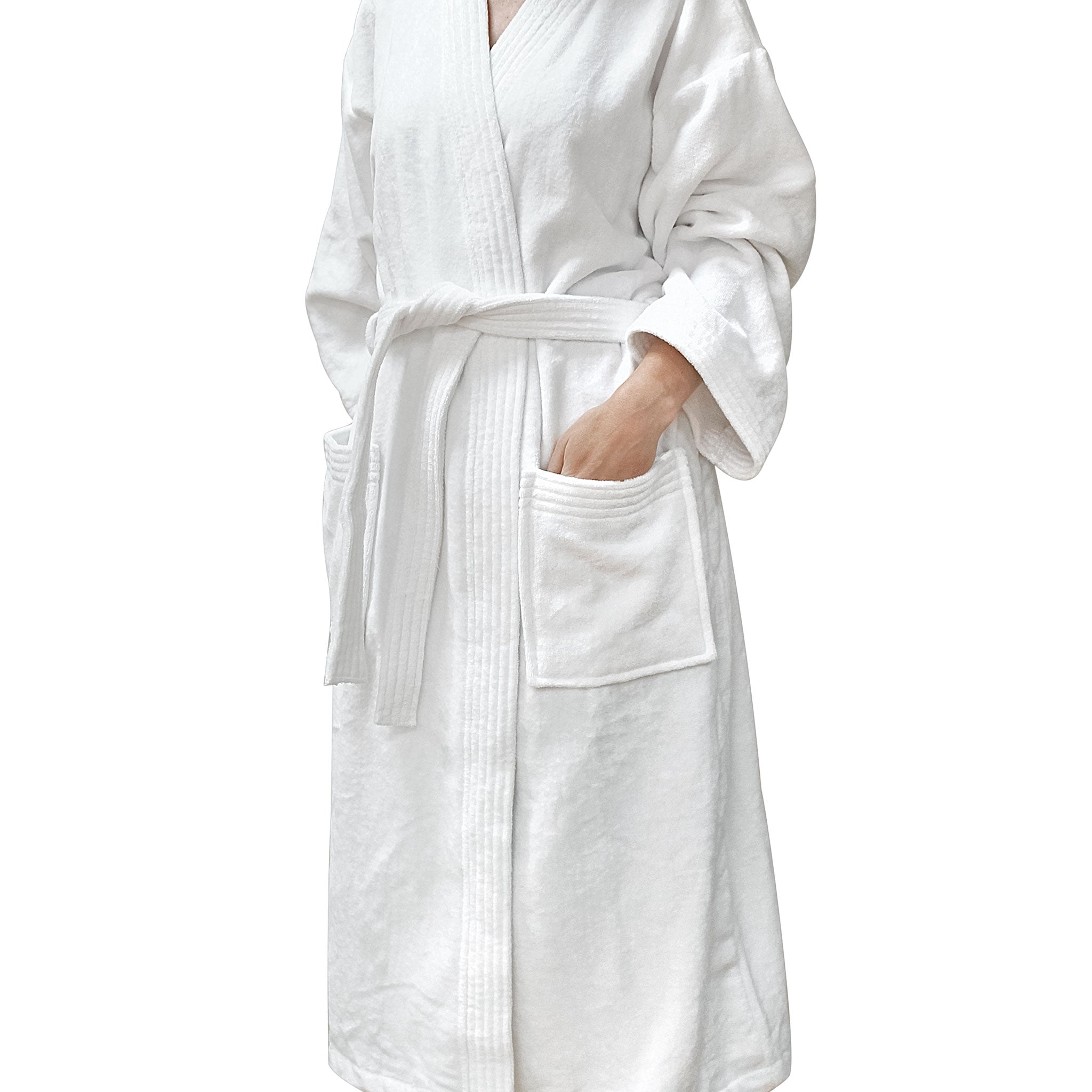 White cotton velour kimono-style bathrobe with a belt tie and patch pockets, modelled with one hand in a pocket against a white background.