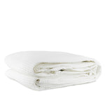 A folded white cotton waffle blanket on a white background.