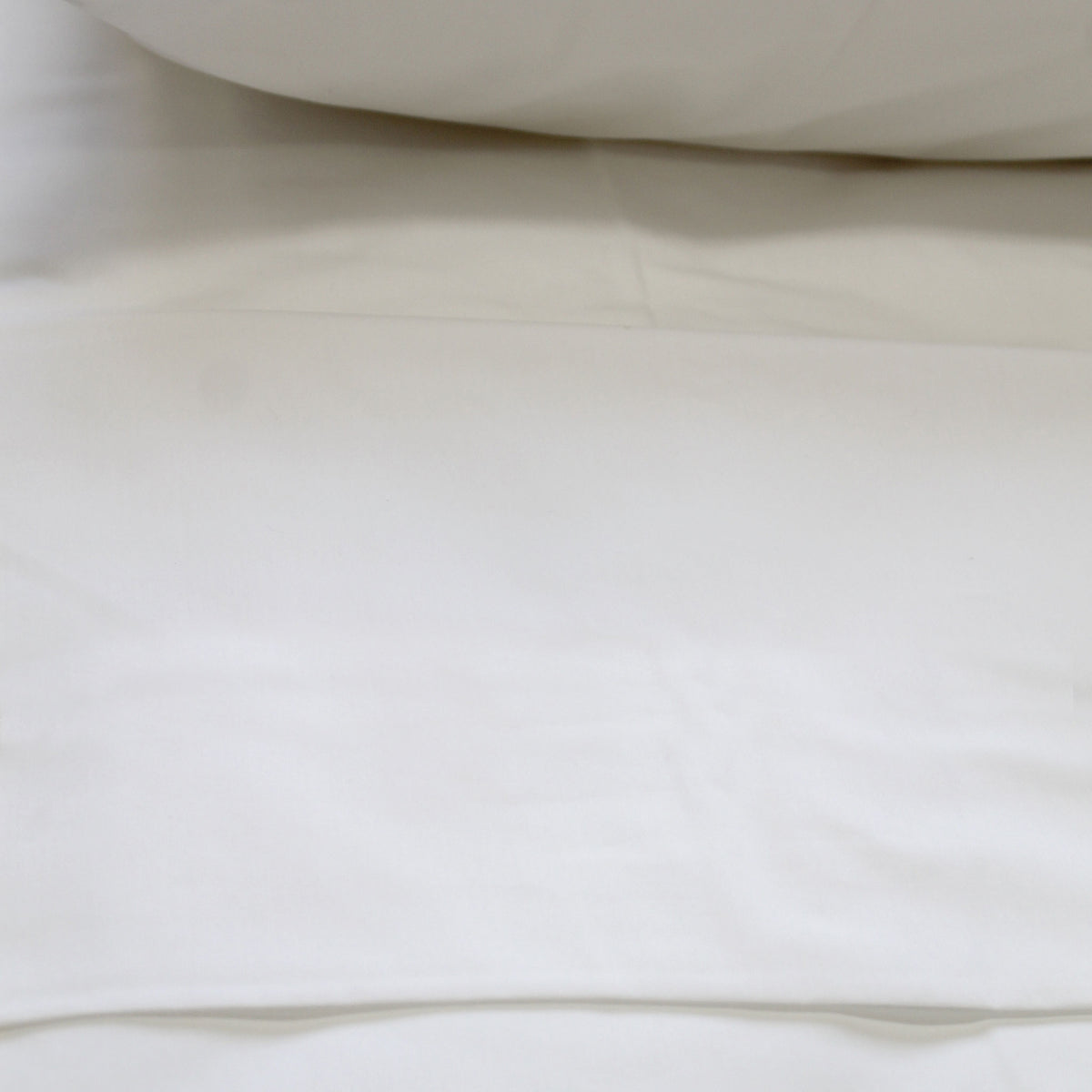 A crisp white flat sheet on a bed, with a pillow visible at the top of the frame.