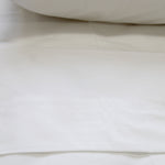 A crisp white flat sheet on a bed, with a pillow visible at the top of the frame.