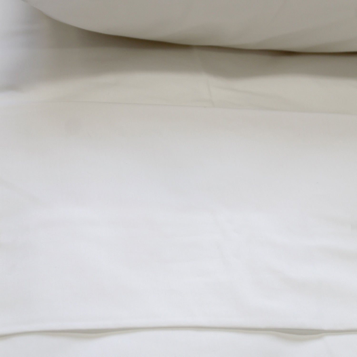 A crisp white flat sheet on a bed, with a pillow visible at the top of the frame.