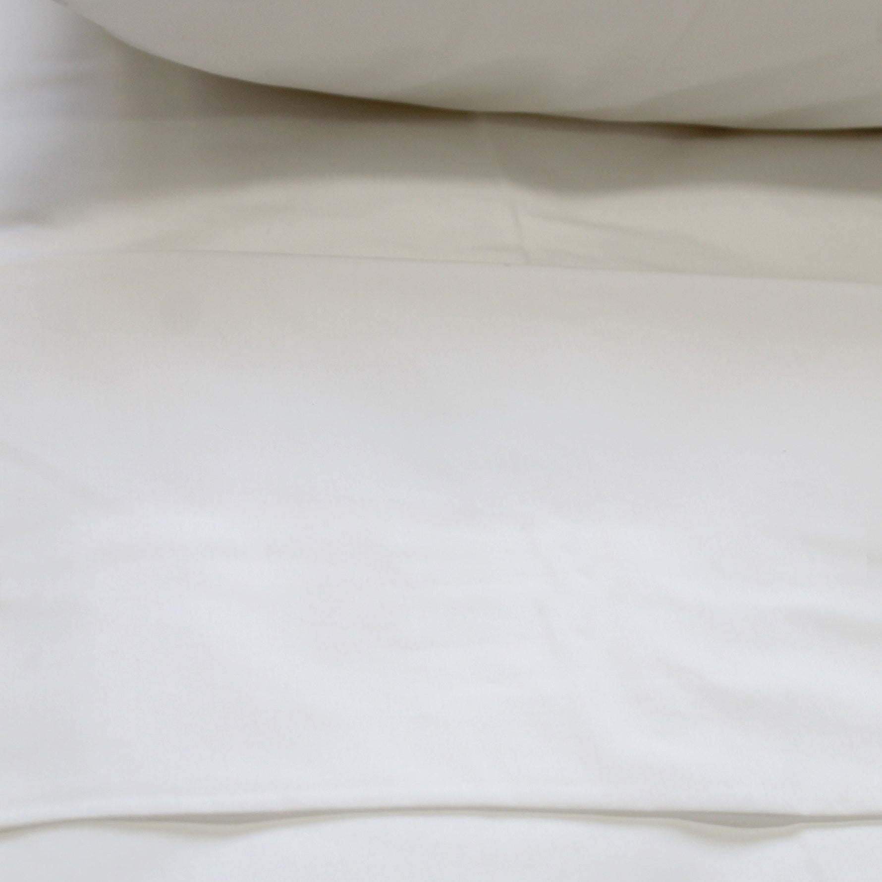 A crisp white flat sheet on a bed, with a pillow visible at the top of the frame.