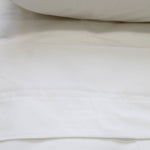 A crisp white flat sheet with a cuff displayed on a bed.