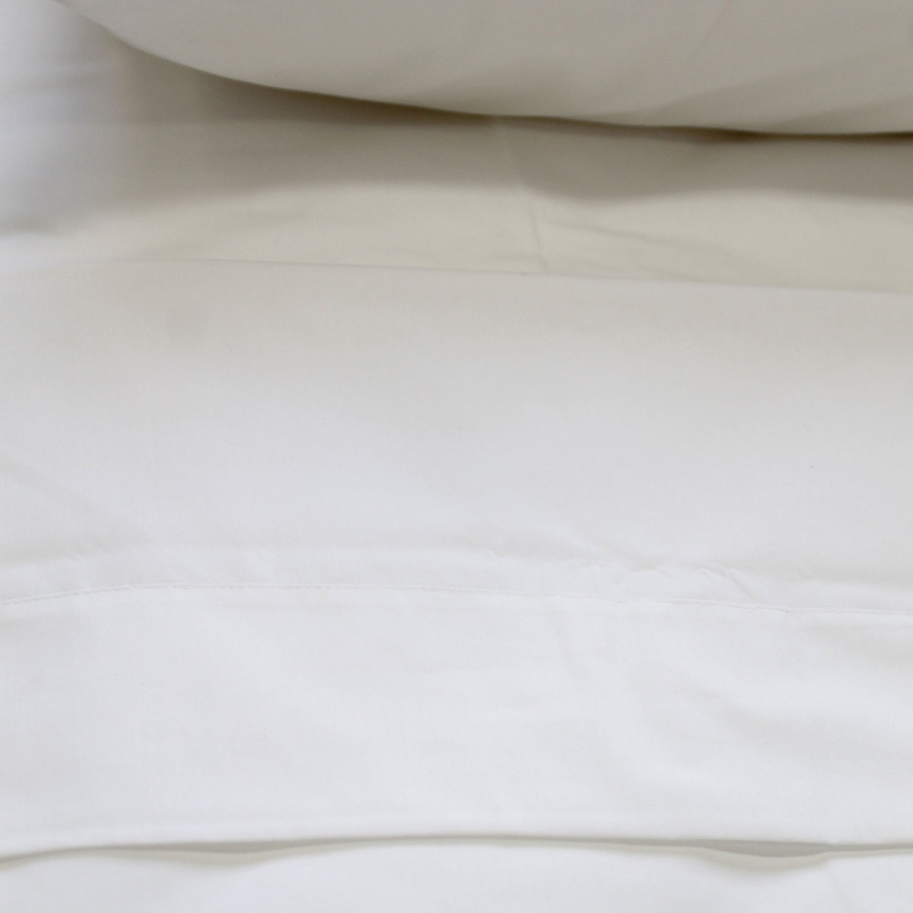 A crisp white flat sheet with a cuff displayed on a bed.