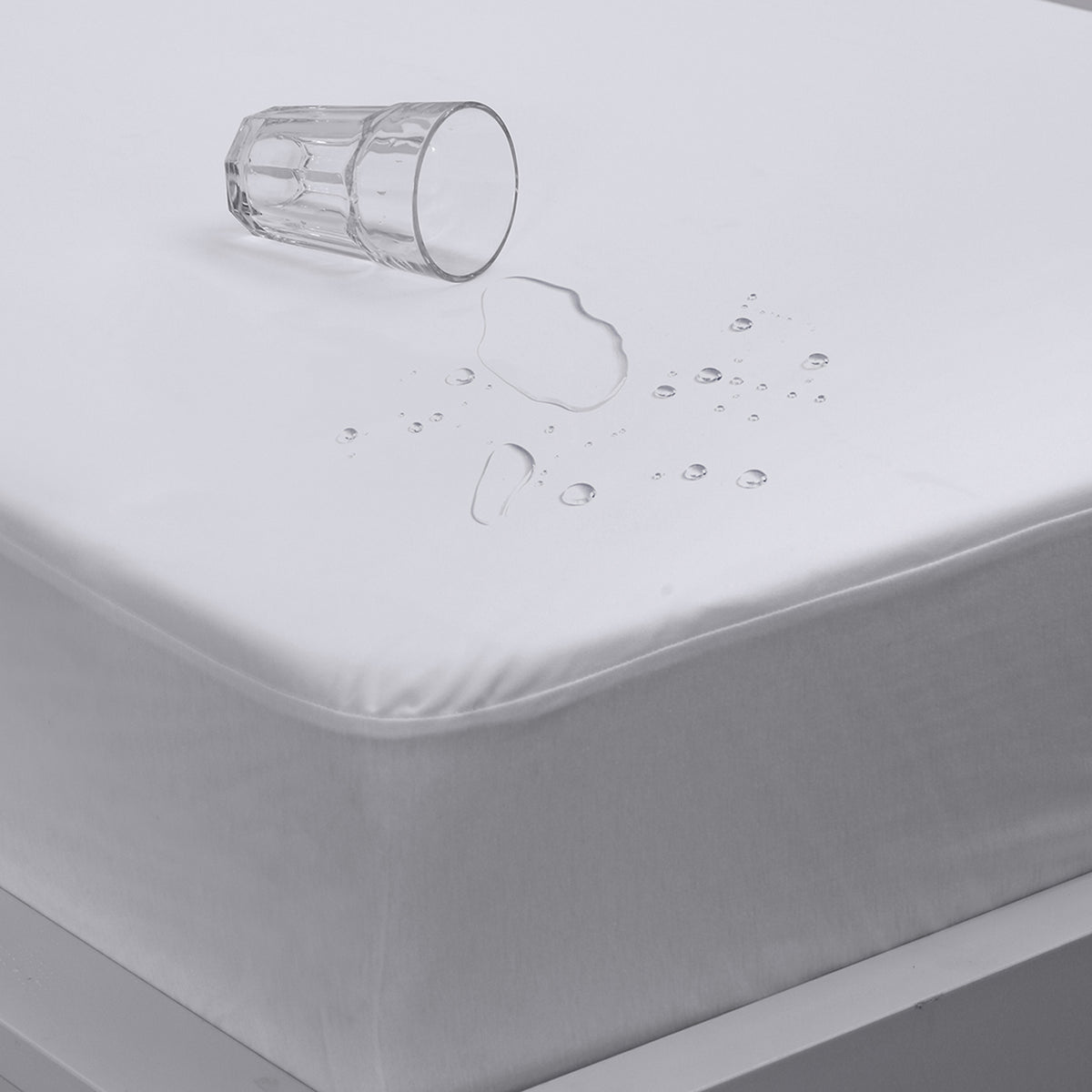 Close-up of a white Eva Clean waterproof mattress protector with water droplets beading on the surface and an overturned glass, fitted over a mattress.