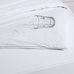 White Eva Clean waterproof quilt protector fitted over a quilt, with an overturned glass and water droplets on the surface to demonstrate waterproof protection.