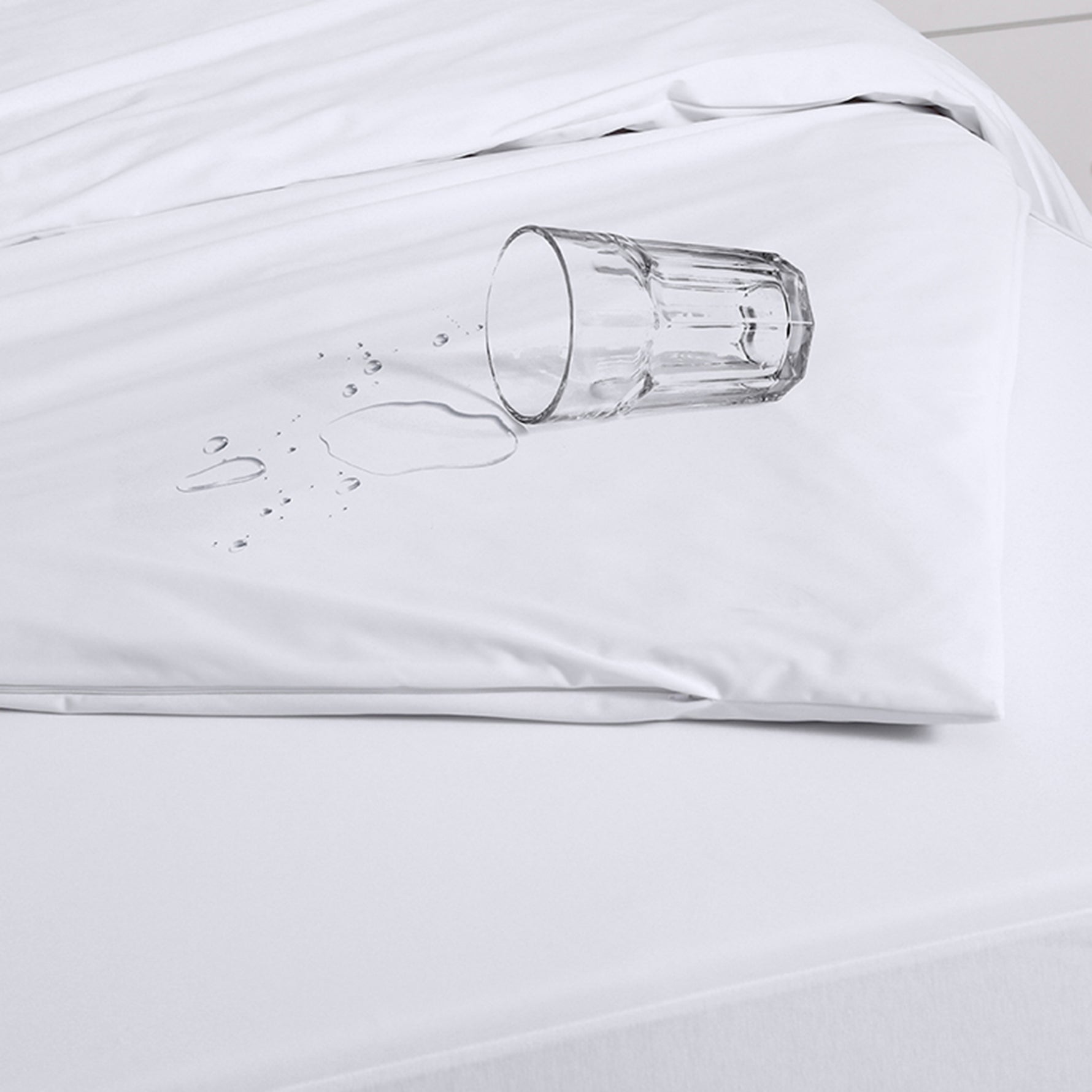 White Eva Clean waterproof quilt protector fitted over a quilt, with an overturned glass and water droplets on the surface to demonstrate waterproof protection.