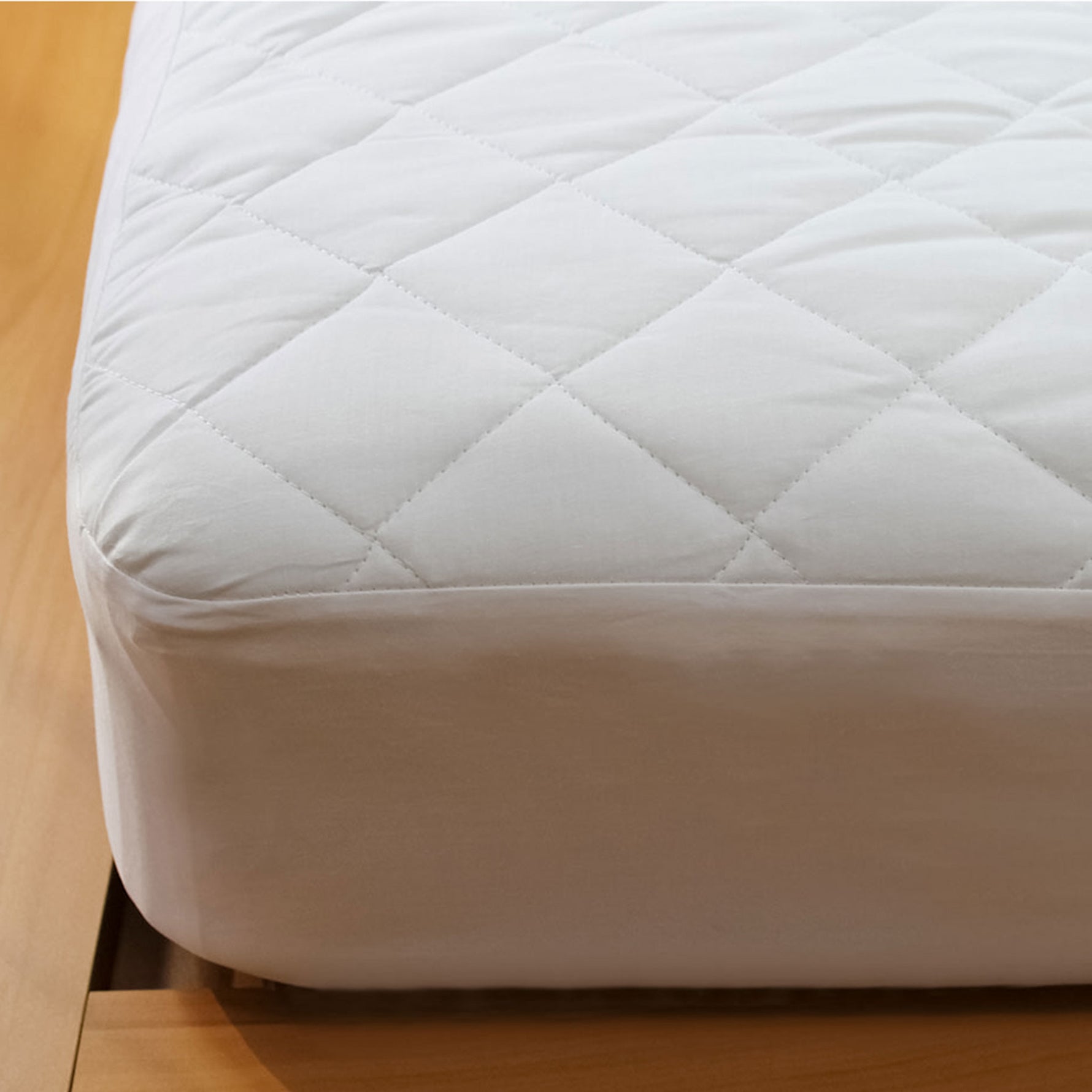 Close-up of a white Hygiene Plus antibacterial mattress protector with a diamond-quilted surface and fitted skirt over a mattress corner.