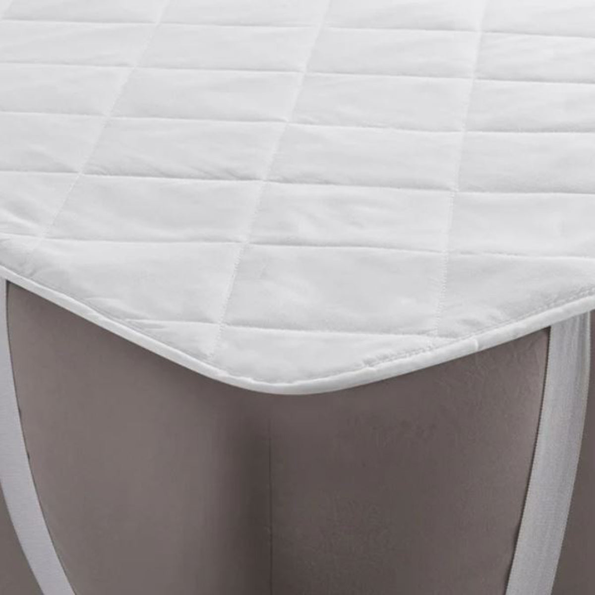 Close-up of a white J-Dream strap-fit mattress protector with diamond quilting and elastic corner straps fitted over a mattress corner.