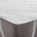 Close-up of a white J-Dream strap-fit mattress protector with diamond quilting and elastic corner straps fitted over a mattress corner.