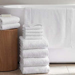 White terry towels stacked beside a bathtub with a matching white bath mat hanging over the edge.