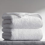 Two folded white terry towels stacked on a marble surface against a soft grey background.
