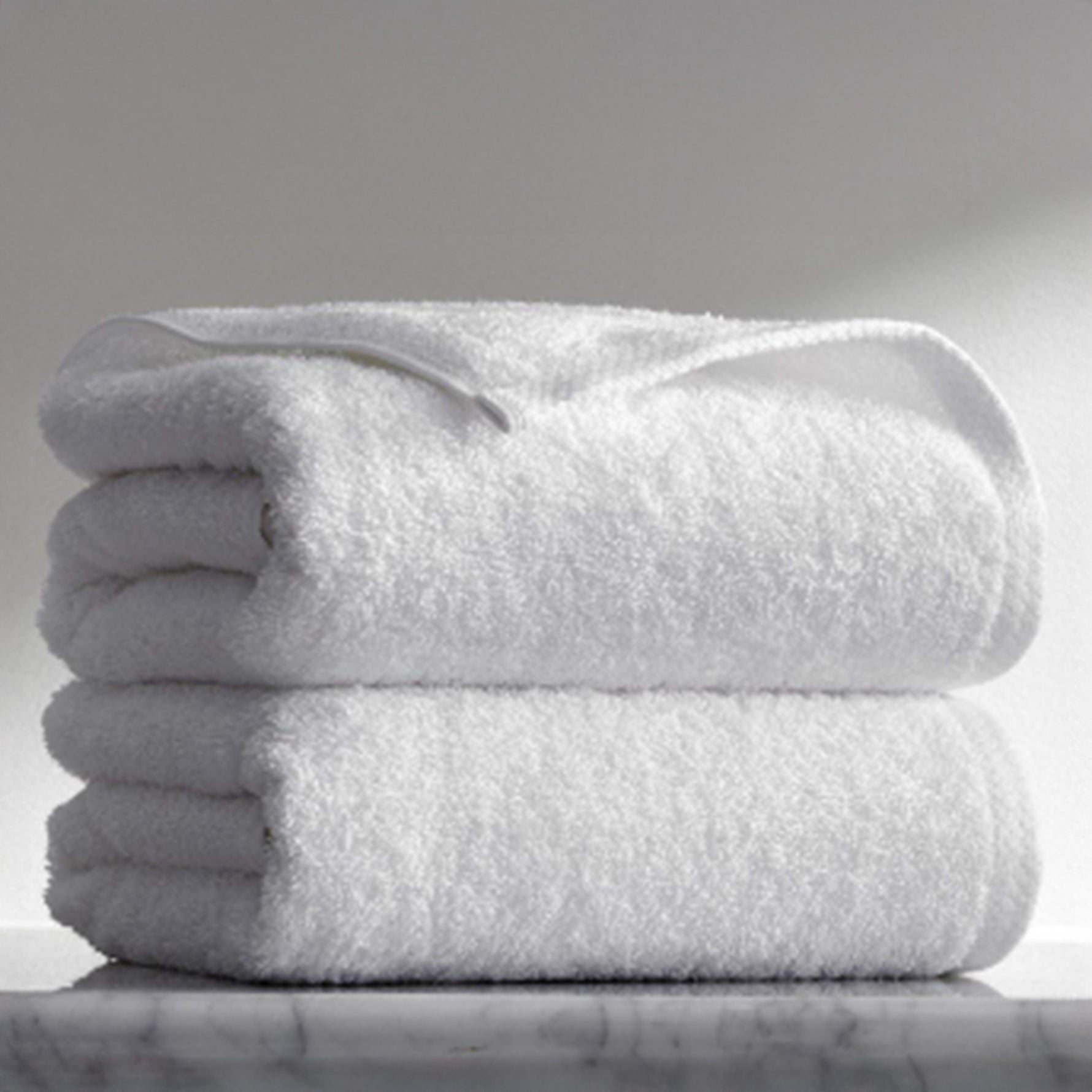 Two folded white terry towels stacked on a marble surface against a soft grey background.