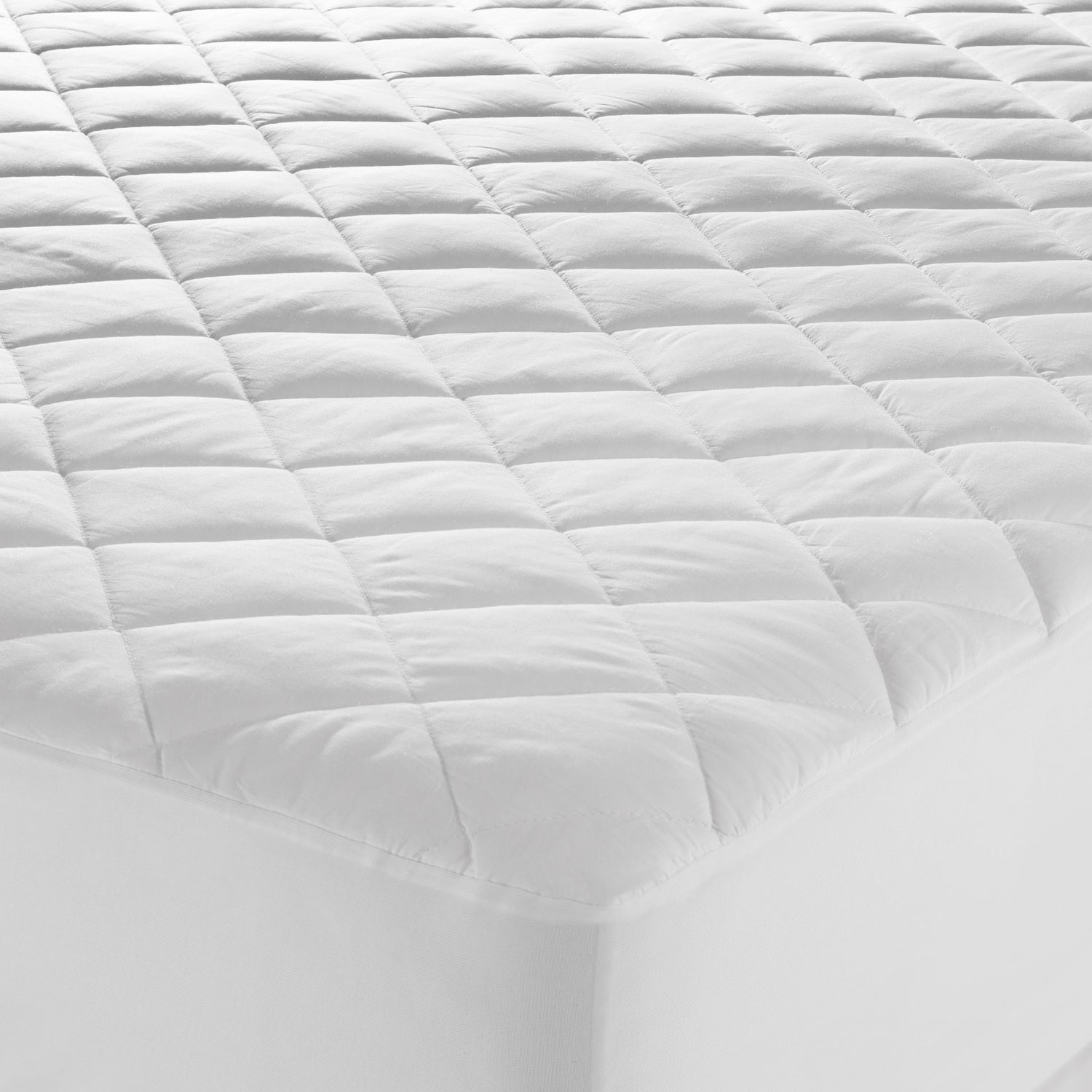 Close-up of a white Microloft mattress protector with a cotton japara cover, diamond-quilted surface and fitted skirt over a mattress corner.