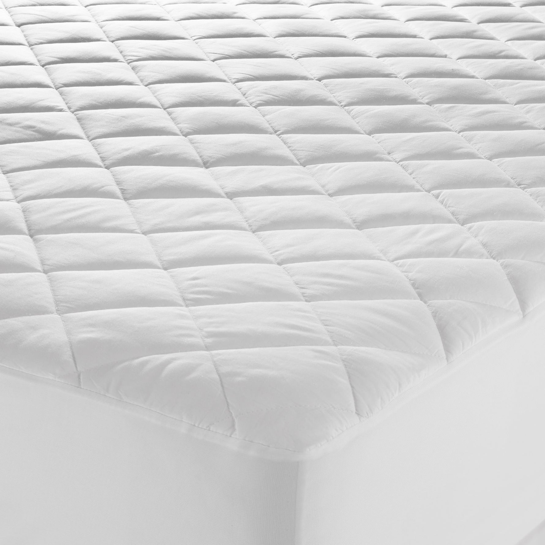 Close-up of a white Microloft mattress protector with a cotton japara cover, diamond-quilted surface and fitted skirt over a mattress corner.