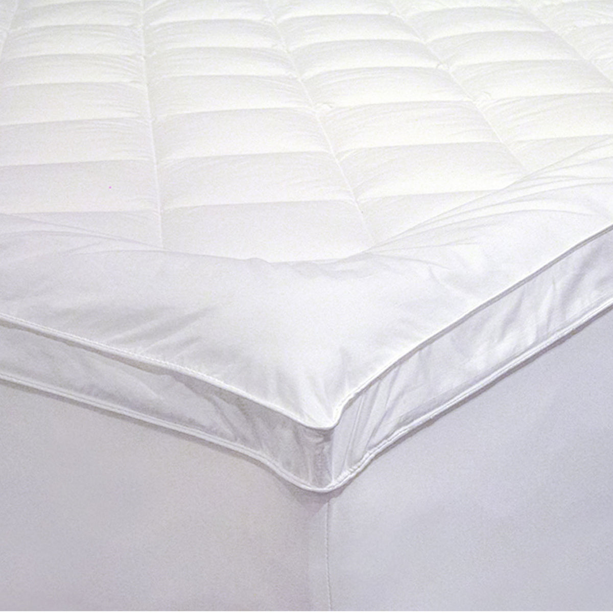 Close-up of a white Microloft gusseted mattress topper with a diamond-quilted centre panel, smooth border, gusseted sidewall and fitted skirt over a mattress corner.
