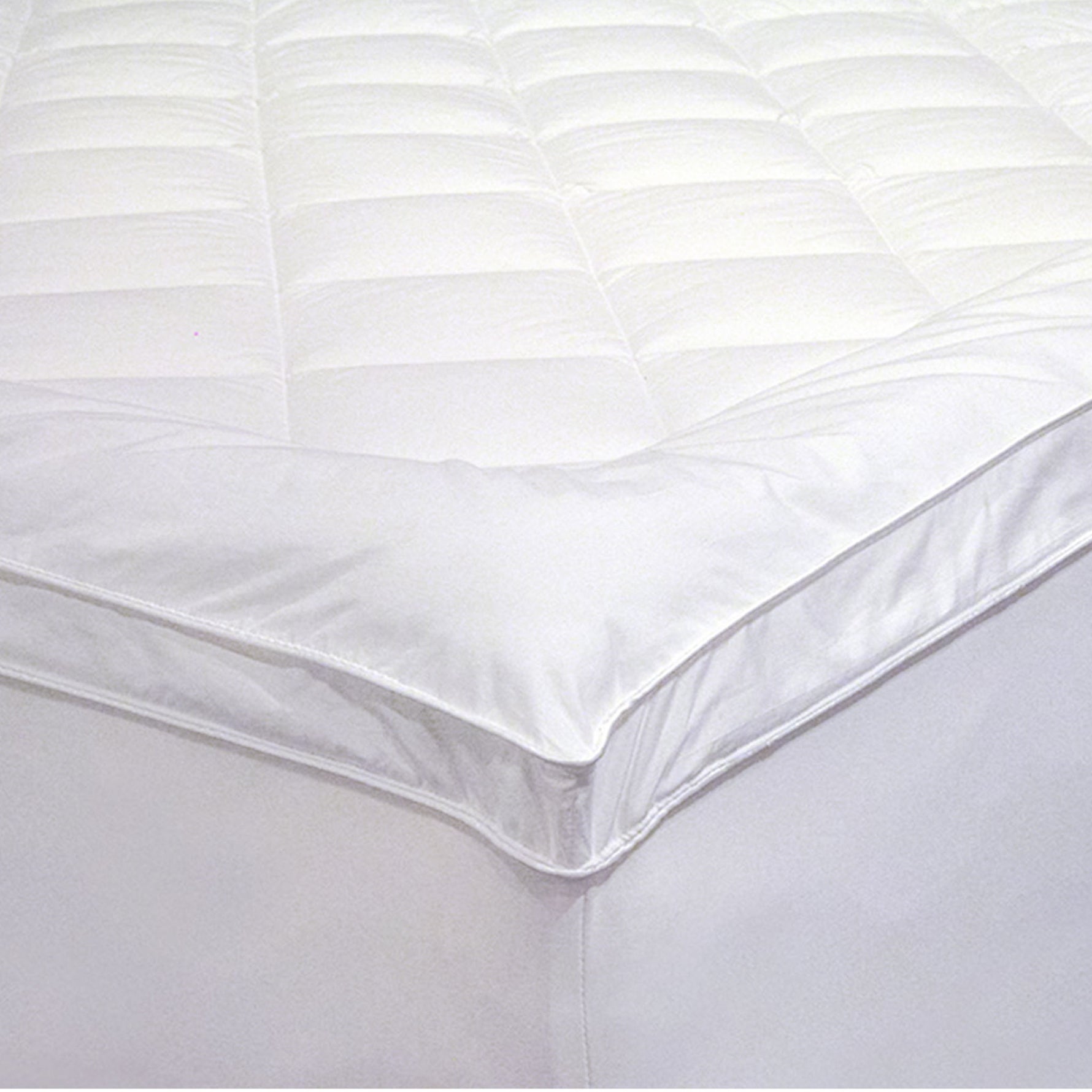 Close-up of a white Microloft gusseted mattress topper with a diamond-quilted centre panel, smooth border, gusseted sidewall and fitted skirt over a mattress corner.
