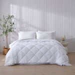 White Repreve all-seasons quilt displayed on a bed in a bedroom setting with a nightstand and potted plant.