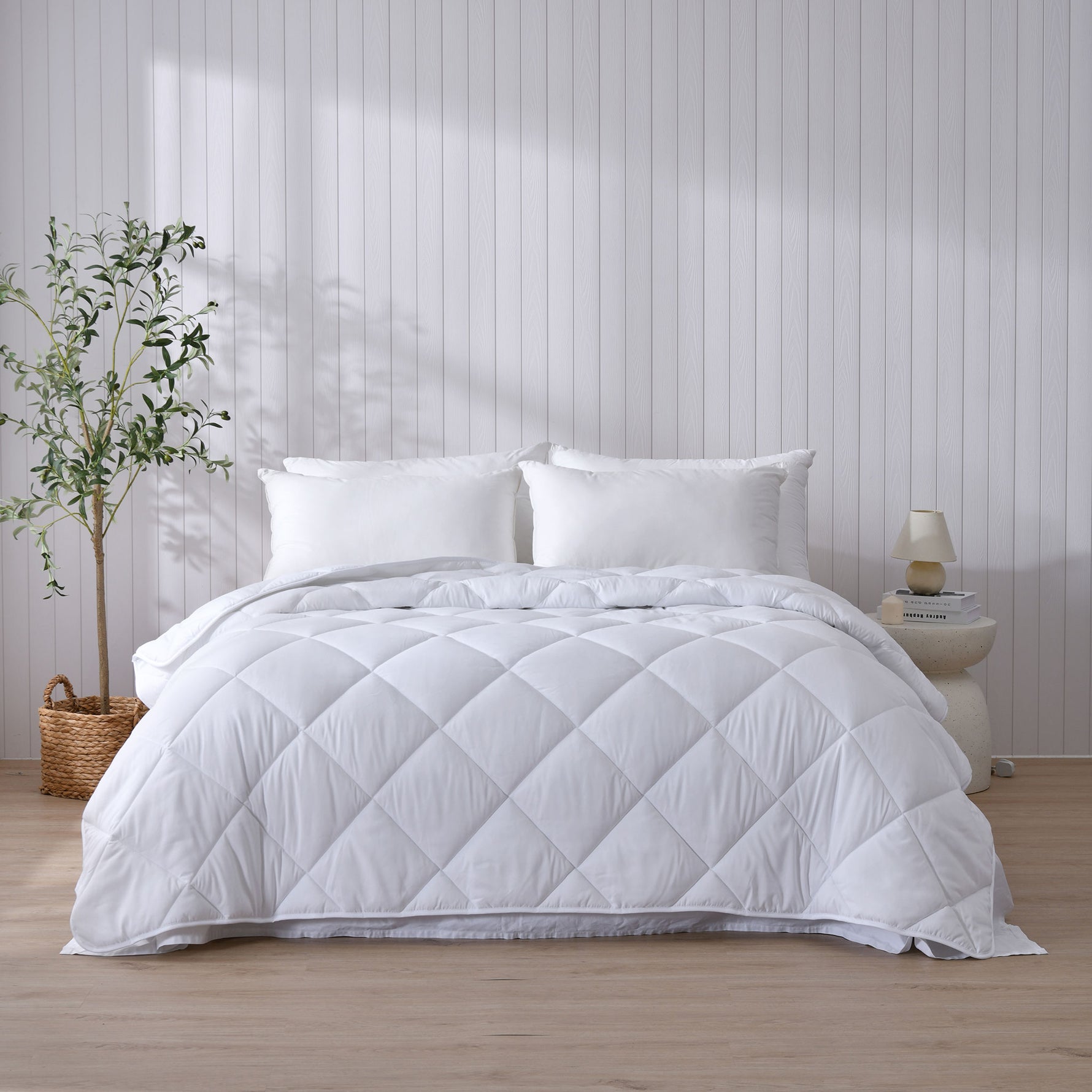 White Repreve all-seasons quilt displayed on a bed in a bedroom setting with a nightstand and potted plant.