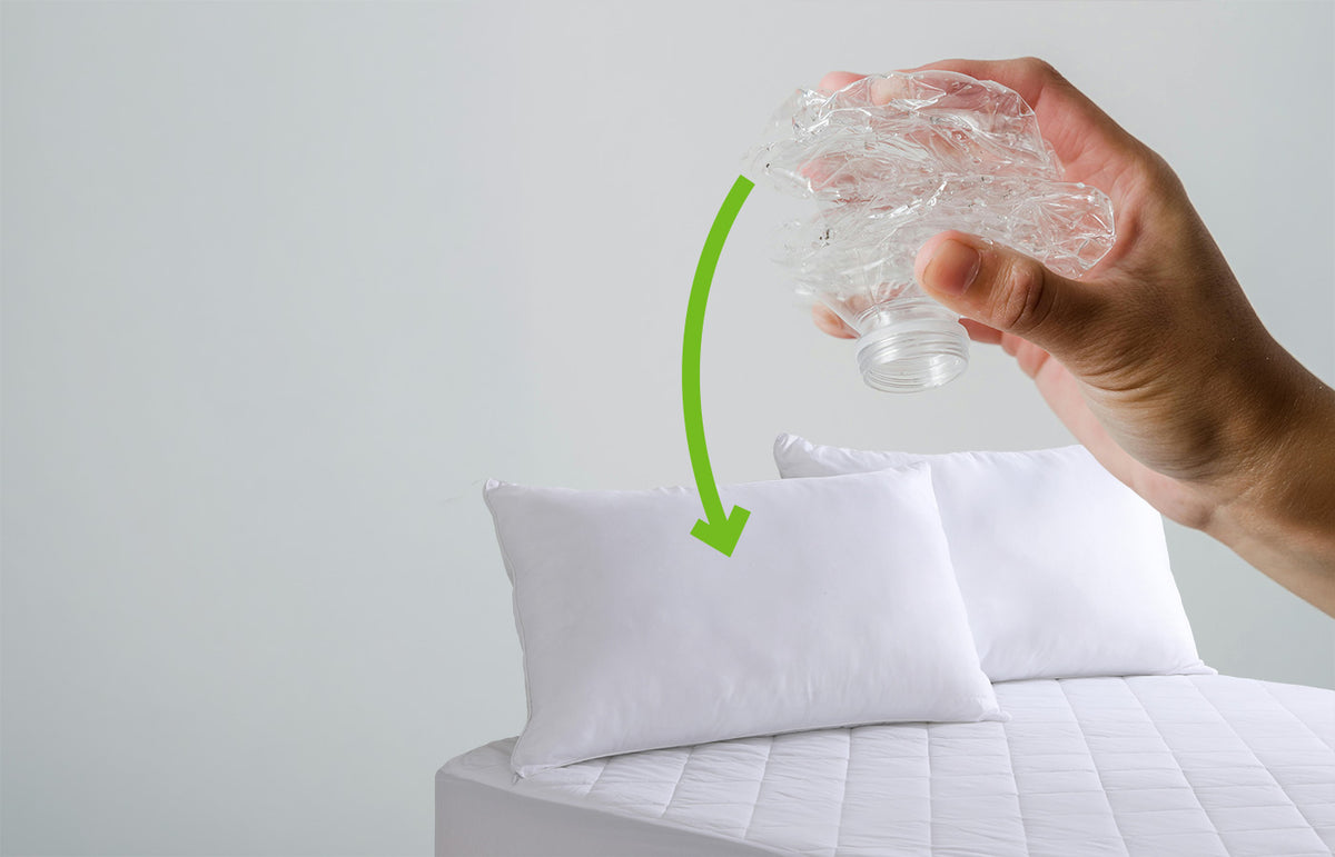 Hand holding a clear plastic bag over a white pillow with a green recycling symbol on a light grey background.