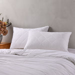White quilted Repreve pillow protectors on pillows displayed on a bed against a grey background.