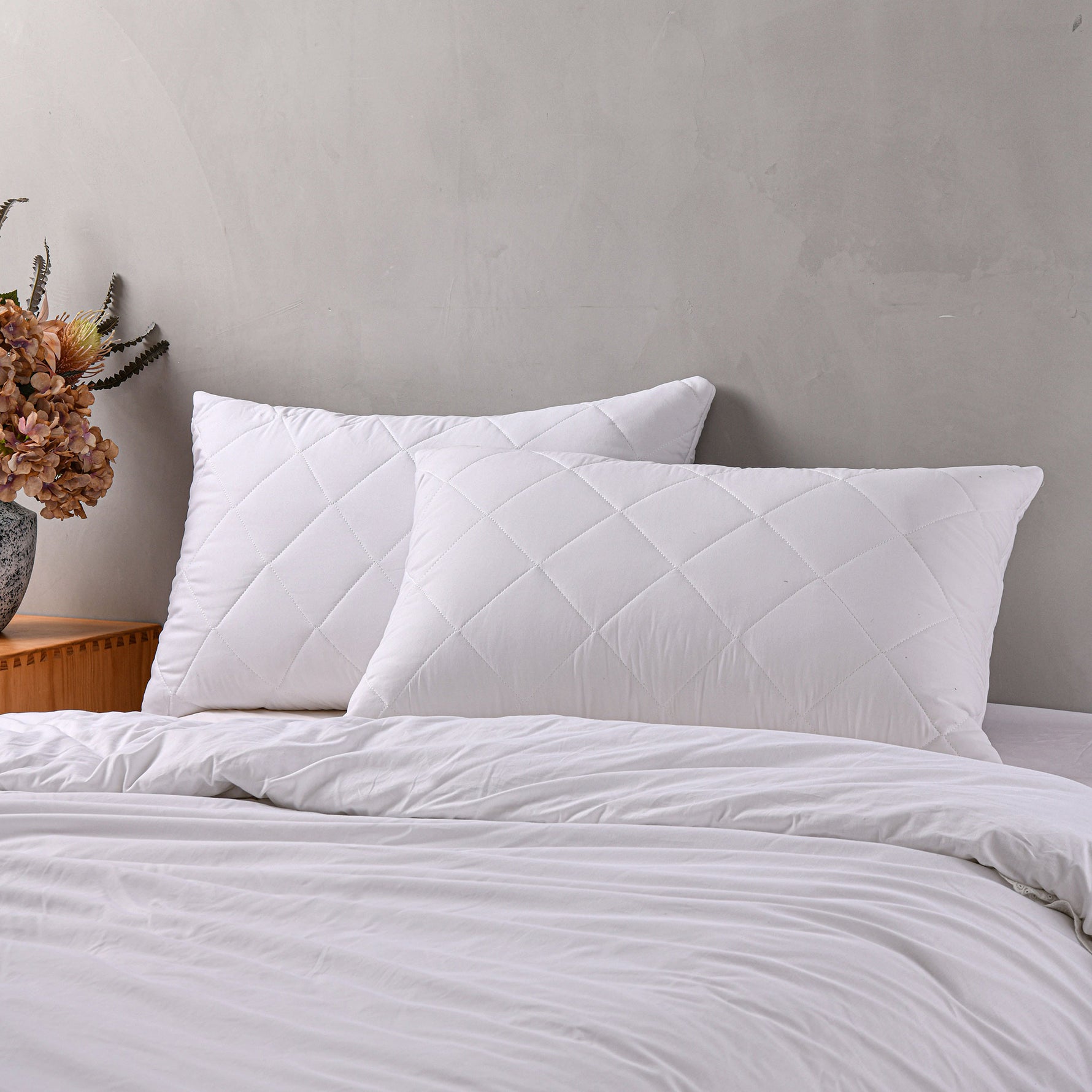 White quilted Repreve pillow protectors on pillows displayed on a bed against a grey background.