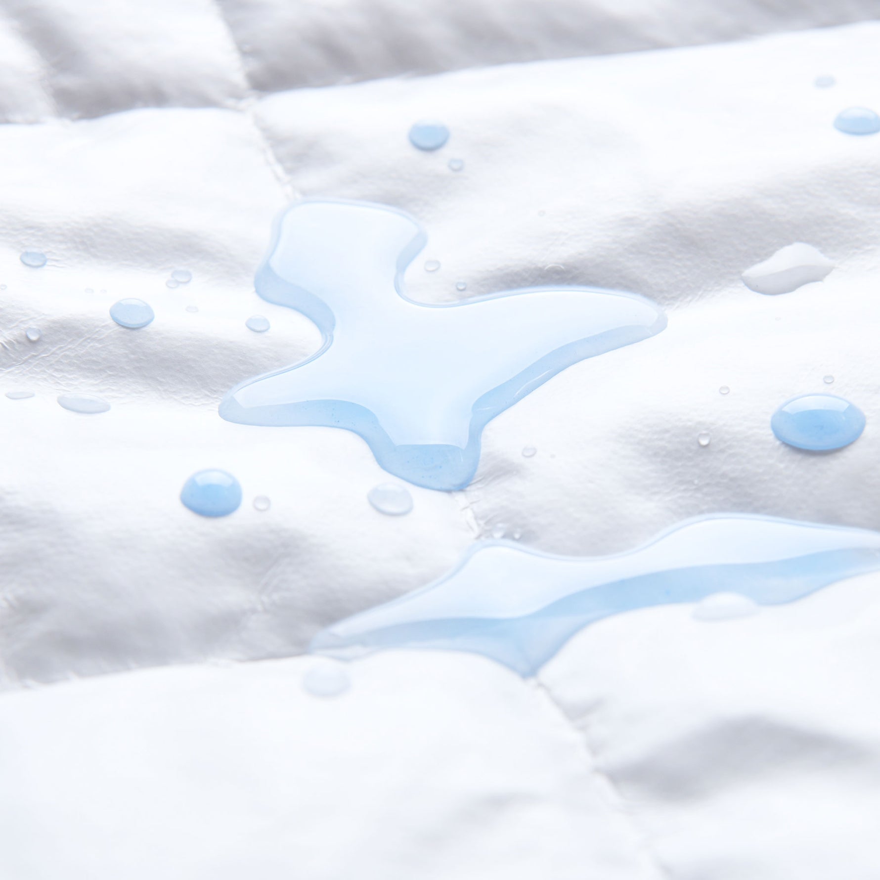 Close-up of white fabric of repreve mattress protector with blue water droplets.