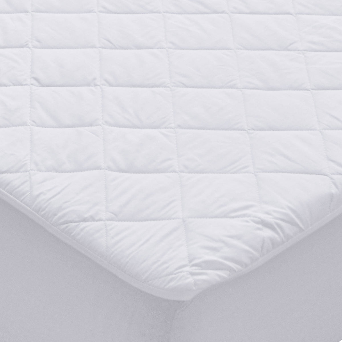 White waterproof Repreve mattress protector with diamond quilting and fitted skirt on a mattress corner.