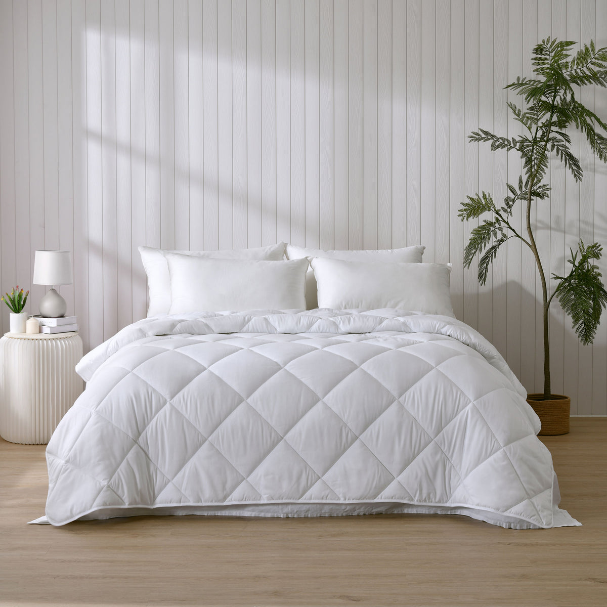 White Repreve winter-weight quilt displayed on a bed in a bedroom setting with a nightstand and potted plant.