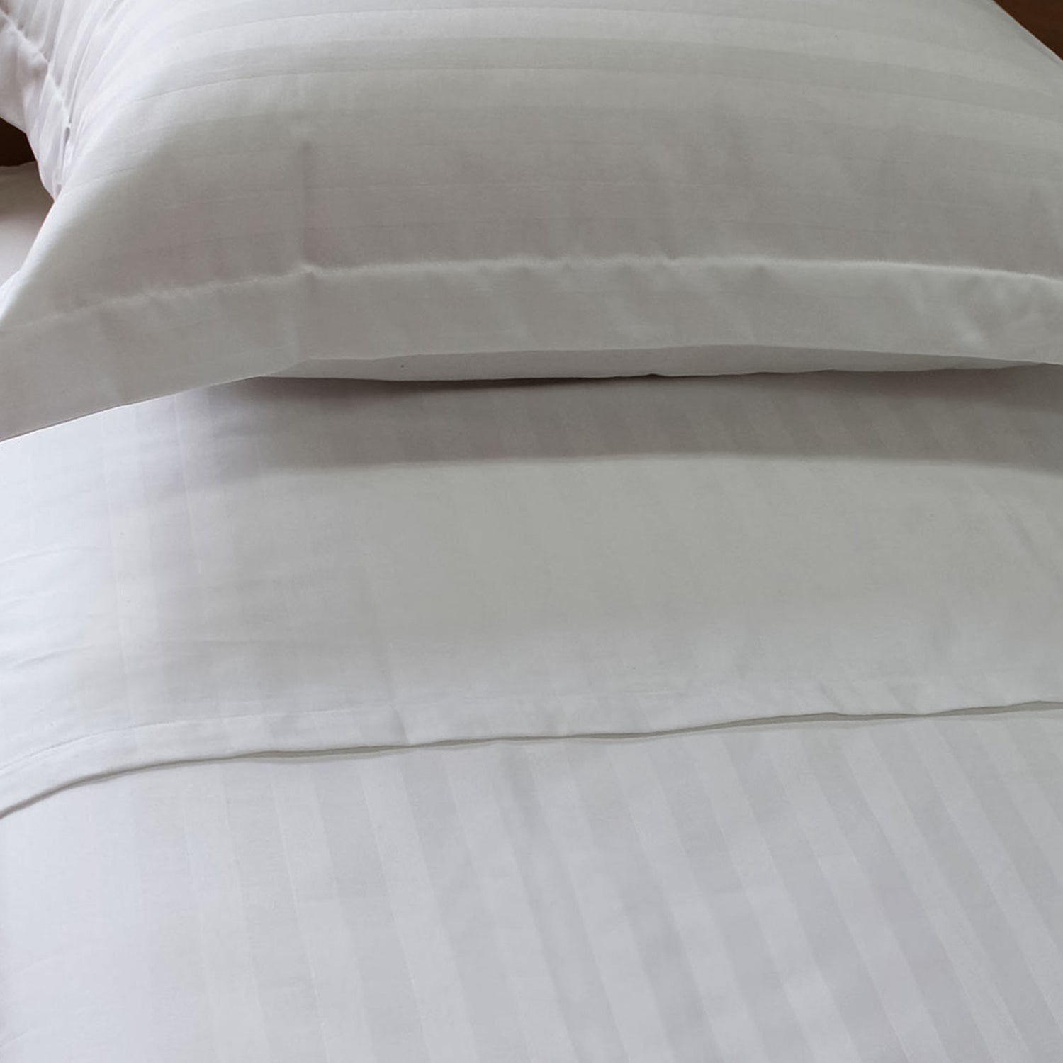 White flat sheet with 2cm jacquard stripes on a bed, with pillows placed on top.