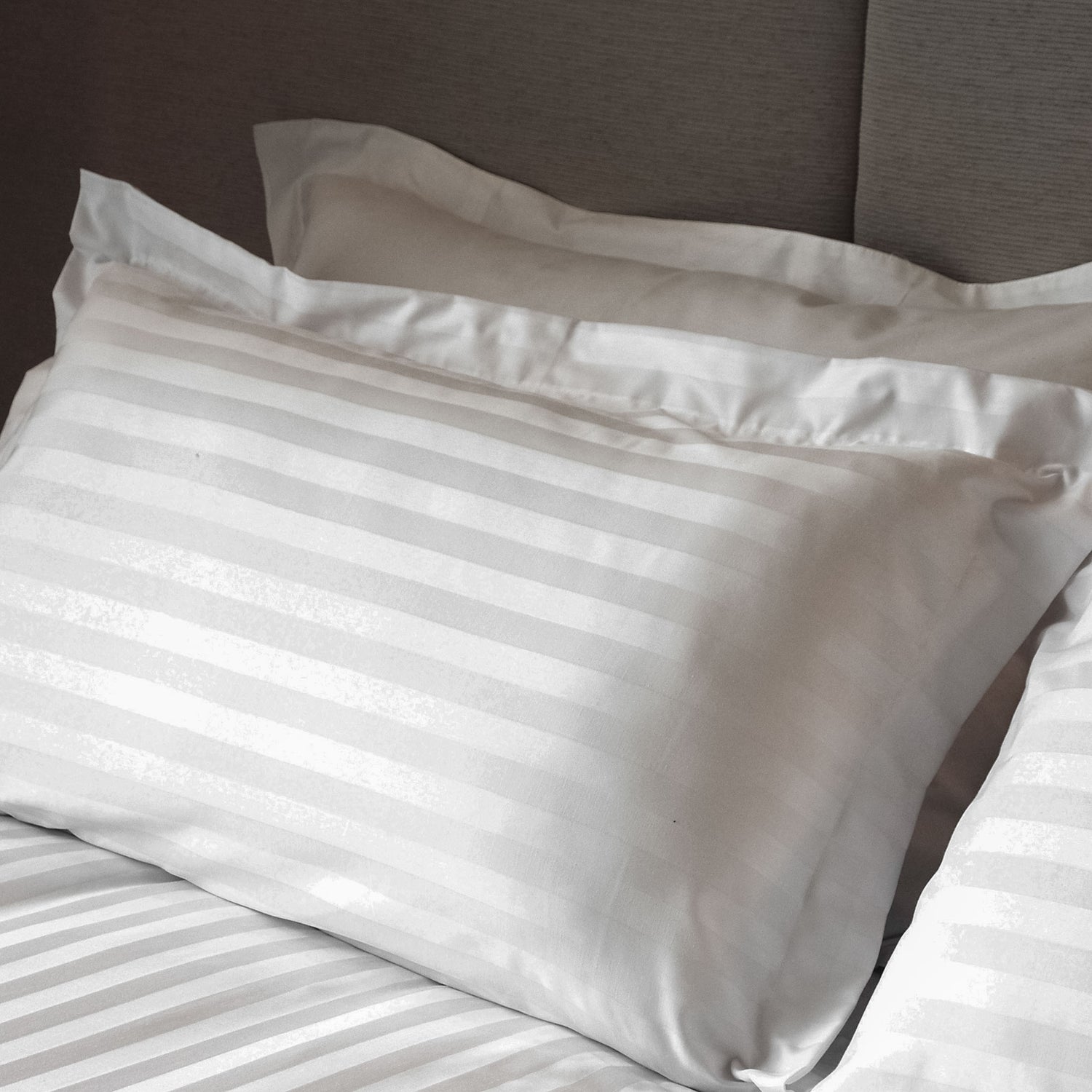 White satin stripe pillowcase with tailored edge fitted over a pillow on a bed.