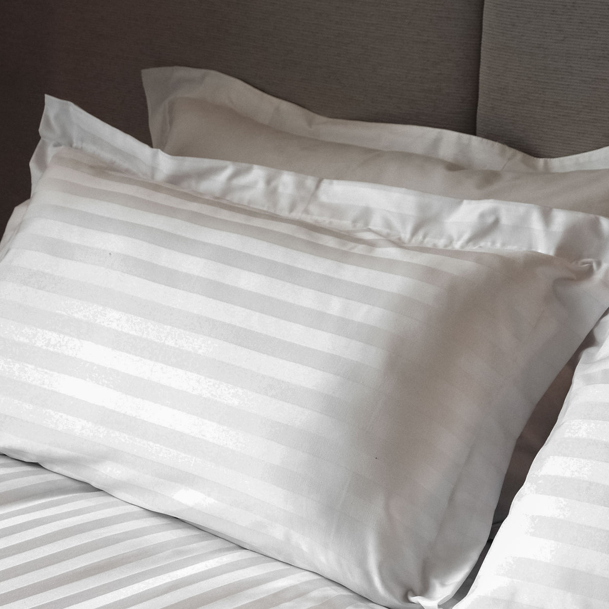 White satin stripe pillowcase with tailored edge fitted over a pillow on a bed.