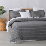 Studio Stripe quilt cover set featuring fine white pinstripes on a slate grey background with matching pillowcases and white pillows on a bed.