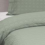 Close-up of a sage green Villa Matelassé coverlet featuring a woven basketweave pattern, with a matching pillow sham in the background.
