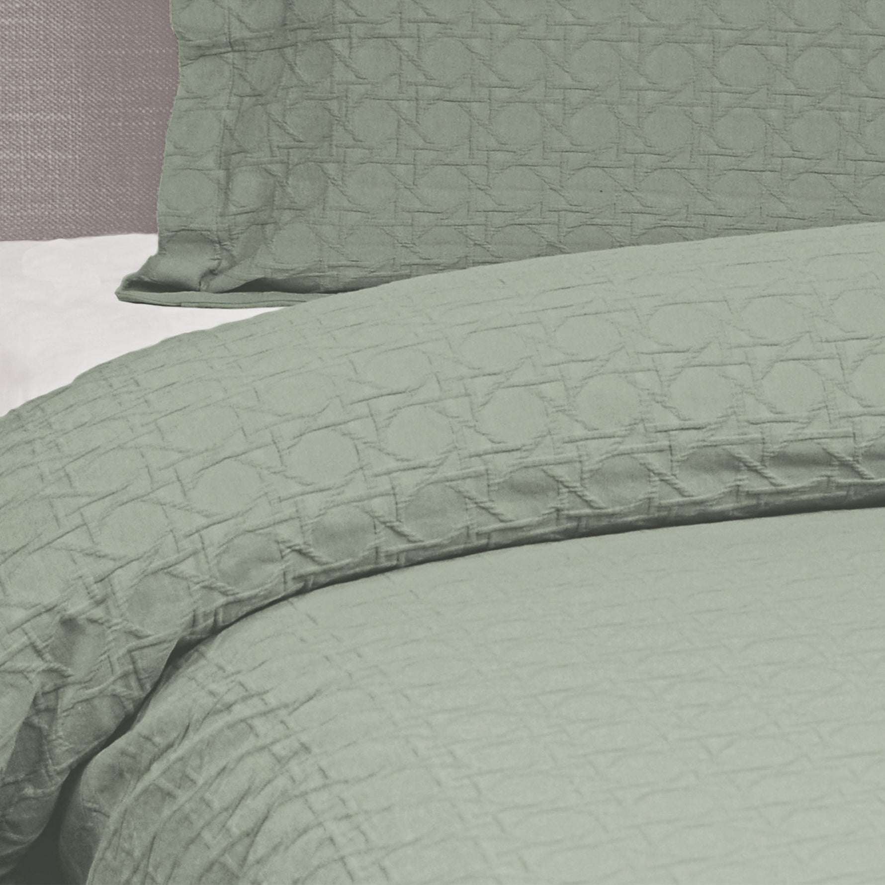 Close-up of a sage green Villa Matelassé coverlet featuring a woven basketweave pattern, with a matching pillow sham in the background.
