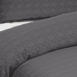 Close-up of a slate grey Villa Matelassé coverlet featuring a woven basketweave pattern, with a matching pillow sham in the background.