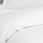 Close-up of a white Villa Matelassé coverlet featuring a woven basketweave pattern, with a matching pillow sham in the background.