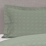 Sage green Villa Matelassé pillow sham featuring a textured woven basketweave pattern and flanged edge, fitted over a pillow on a bed.