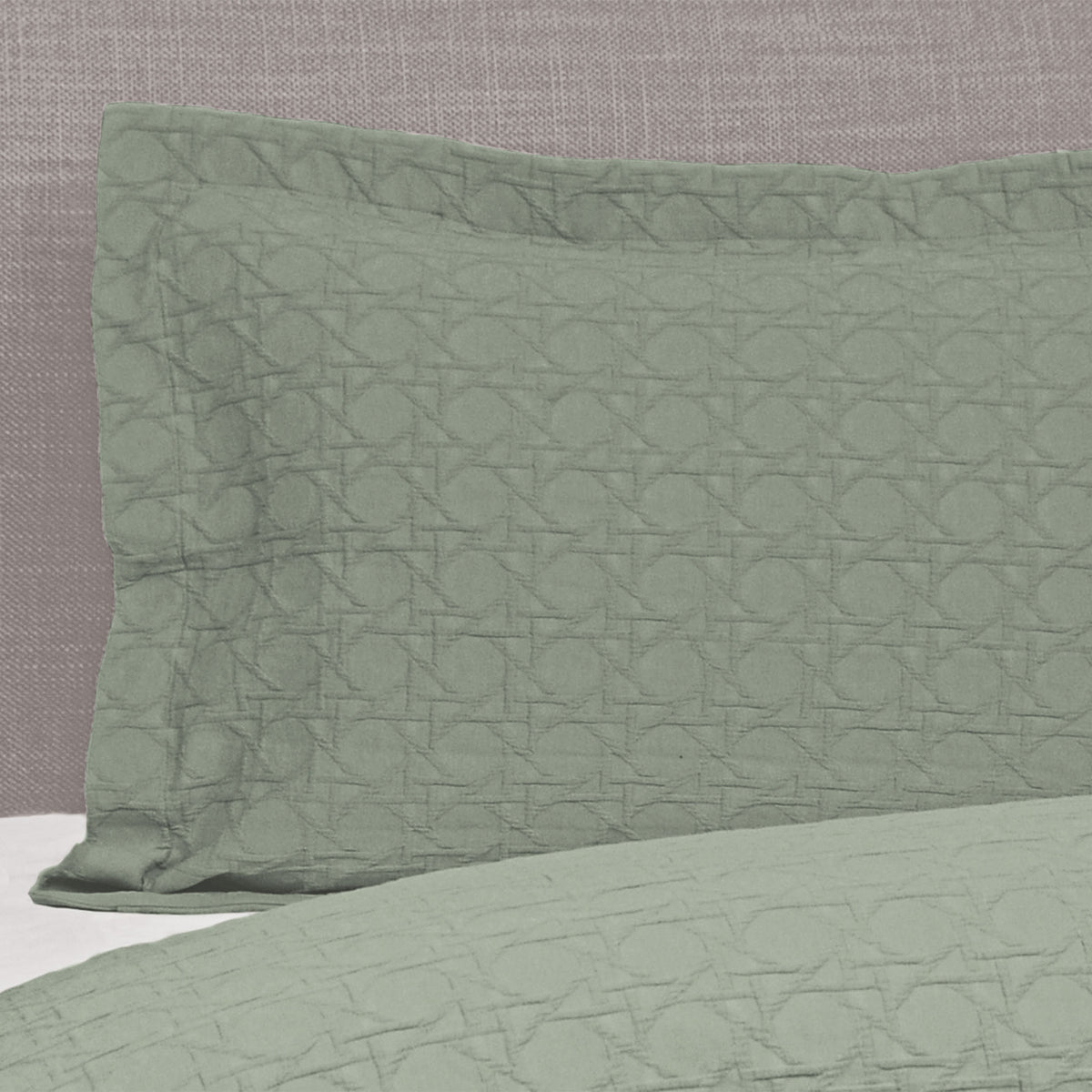 Sage green Villa Matelassé pillow sham featuring a textured woven basketweave pattern and flanged edge, fitted over a pillow on a bed.