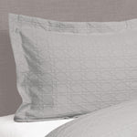 Silver grey Villa Matelassé pillow sham featuring a textured woven basketweave pattern and flanged edge, fitted over a pillow on a bed.