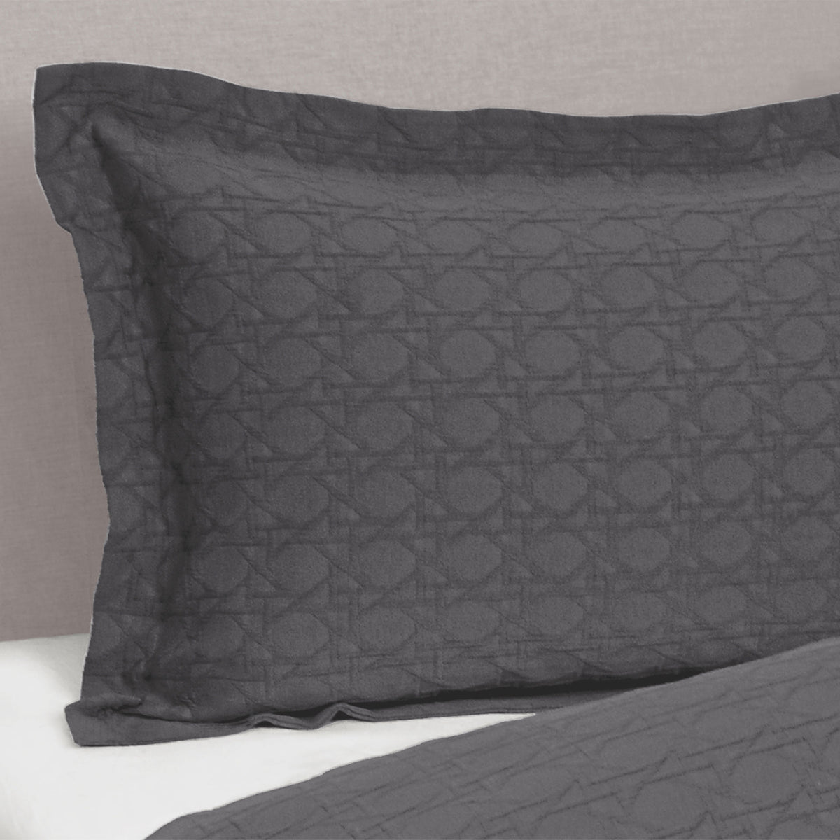 Slate grey Villa Matelassé pillow sham featuring a textured woven basketweave pattern and flanged edge, fitted over a pillow on a bed.