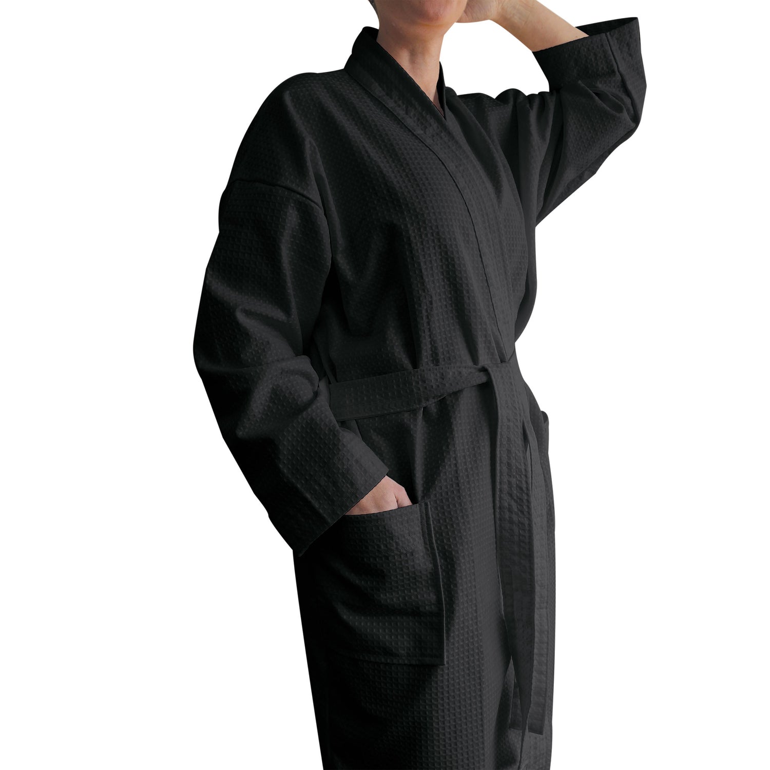 Black waffle-weave kimono-style bathrobe with a belt tie and patch pockets, modelled with one hand in a pocket against a white background.