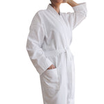 White waffle-weave kimono-style bathrobe with a belt tie and patch pockets, modelled with one hand in a pocket against a white background.